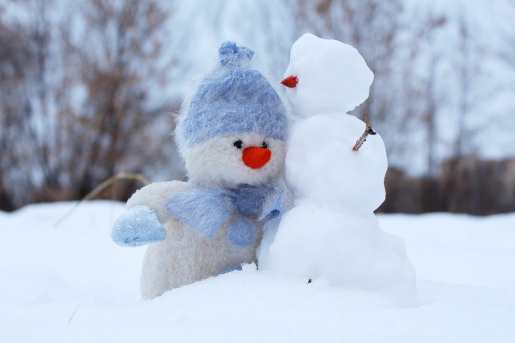  un petit bonhomme de neige et une peluche dehors dans la neige